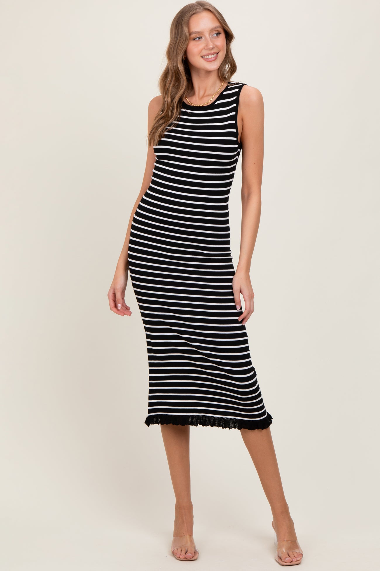 woman wearing a black and white striped sleeveless midi dress with fringe hem and posing with one hand on her hip
