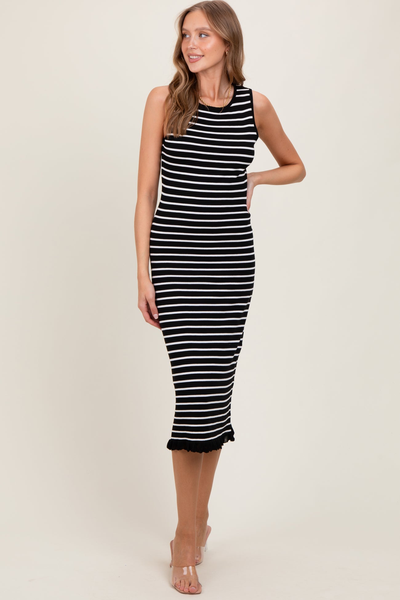 woman wearing a black and white striped sleeveless midi dress with ruffled hem and a fitted silhouette