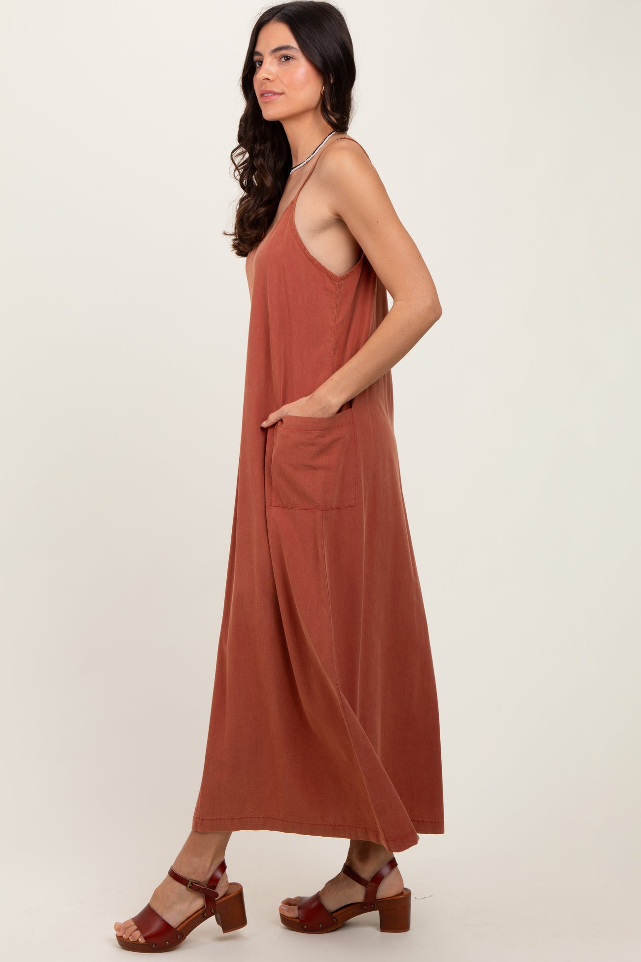 woman wearing a rust-colored sleeveless maxi dress with side pockets and strappy sandals