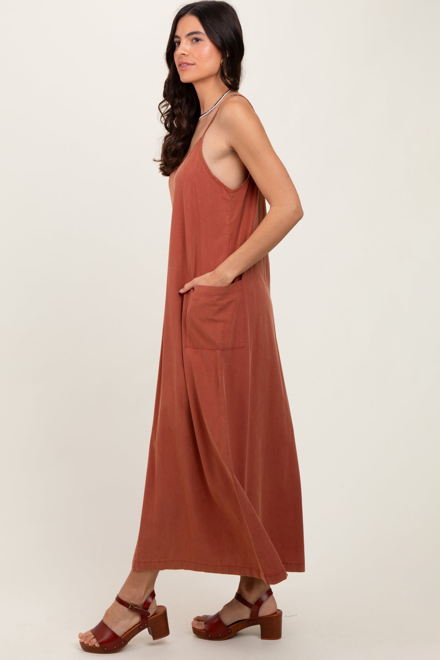 woman wearing a rust-colored sleeveless maxi dress with side pockets and strappy sandals