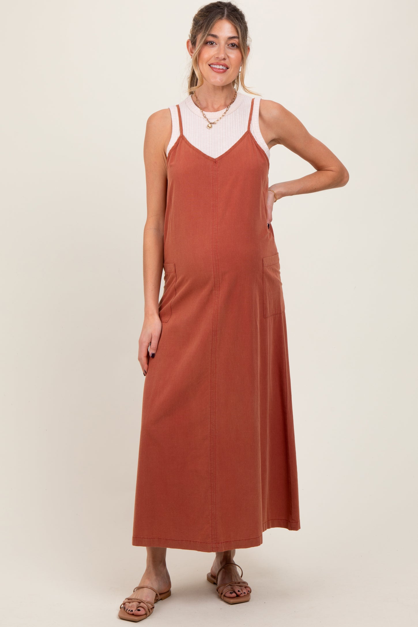 woman wearing a rust-colored maternity maxi dress over a white ribbed tank top, showing her baby bump