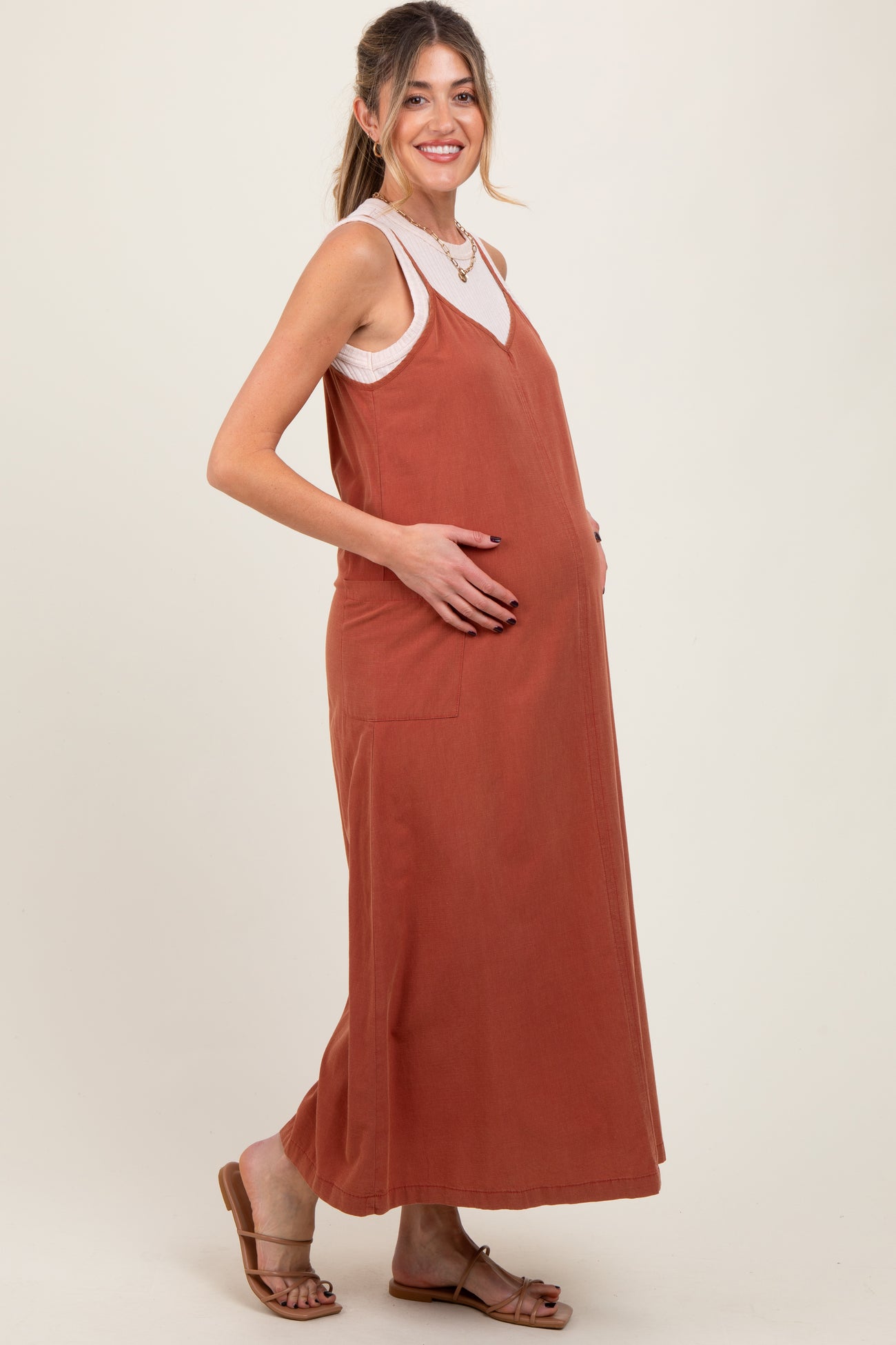 woman wearing a rust-colored maternity maxi dress and cradling her baby bump