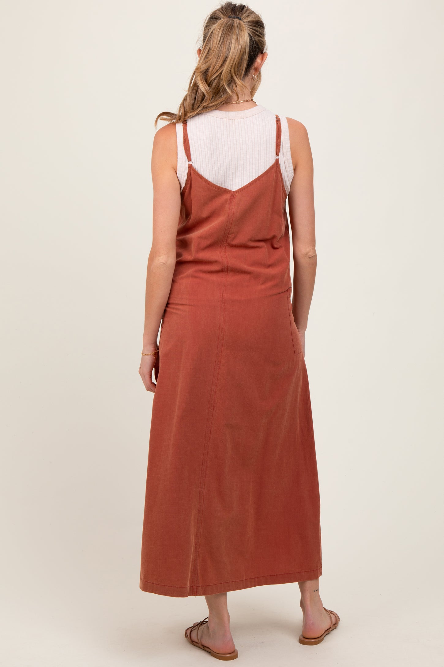woman wearing an rust colored maternity maxi dress with spaghetti straps and a relaxed fit, showing the back view