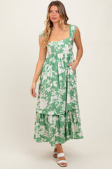 woman wearing a green floral maxi dress with a square neckline and tiered skirt, posing with hands in pockets