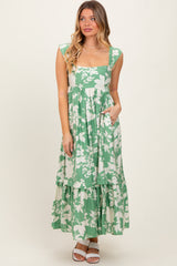 woman wearing a green floral print maxi dress with a square neckline and tiered skirt, posing with hands in pockets
