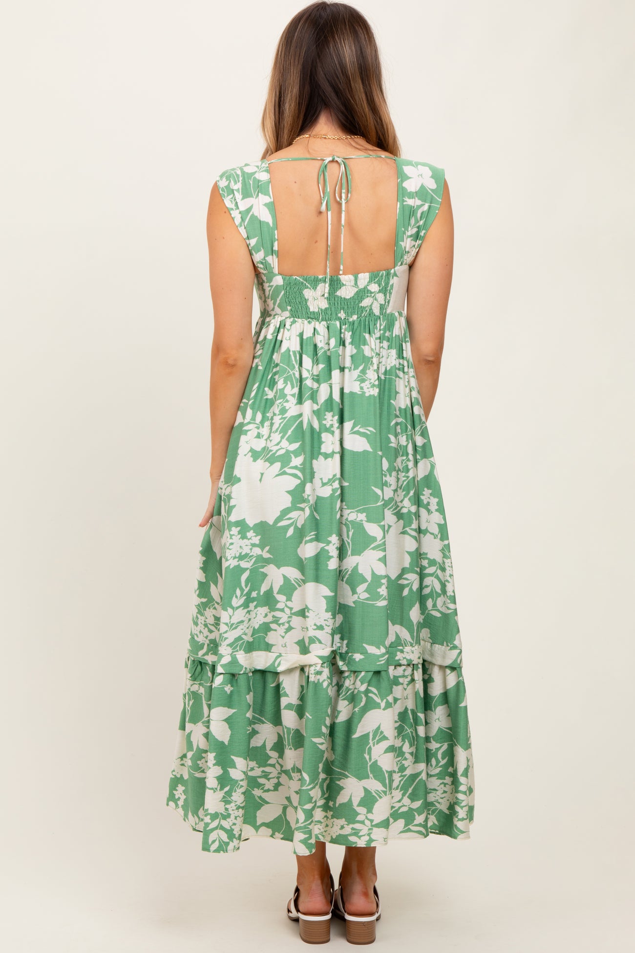 woman wearing a green floral maxi dress with a tiered skirt and an open back detail