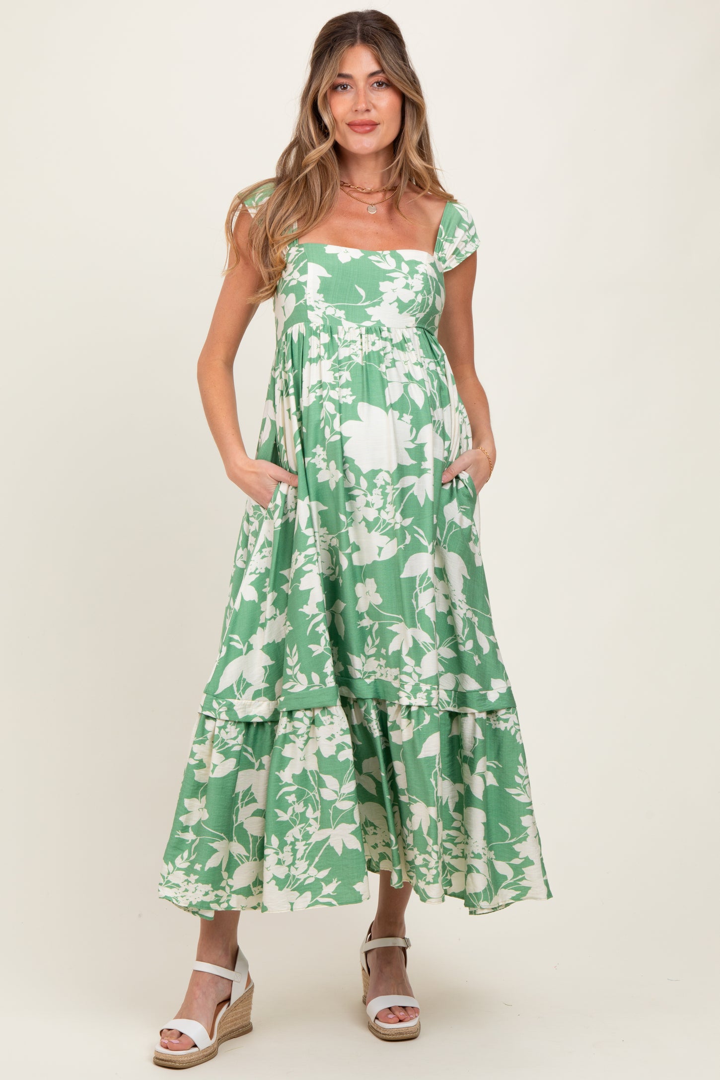 woman wearing a green floral print maternity dress with a tiered skirt and pockets