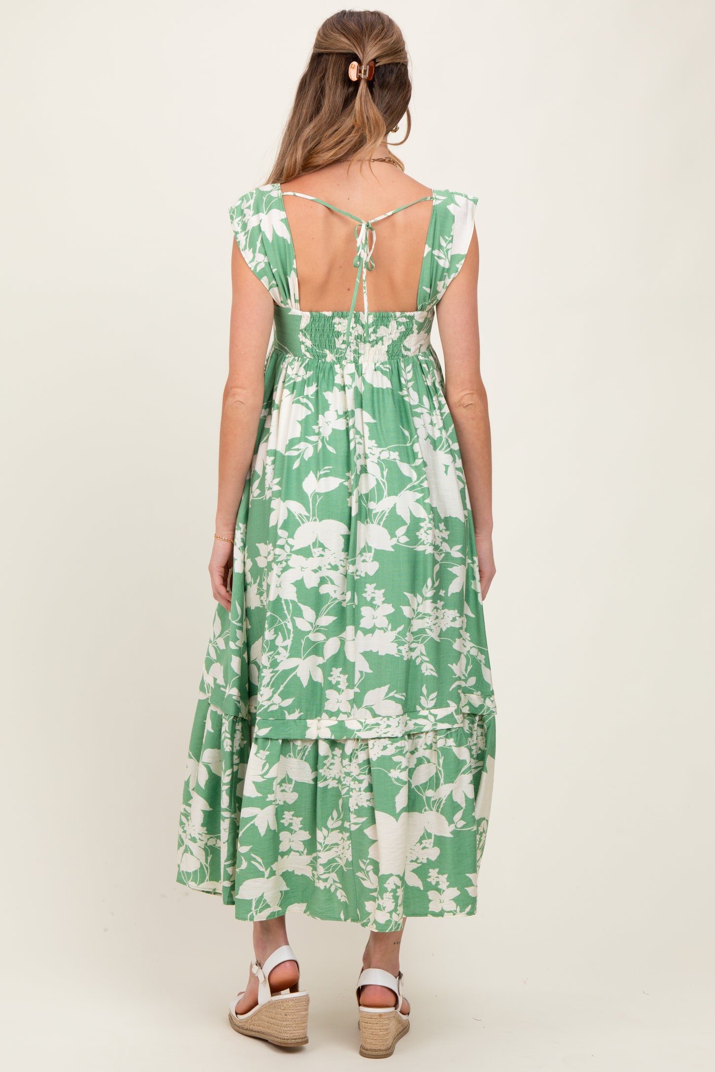 woman wearing a green floral maternity maxi dress with a tie back and ruffled hem