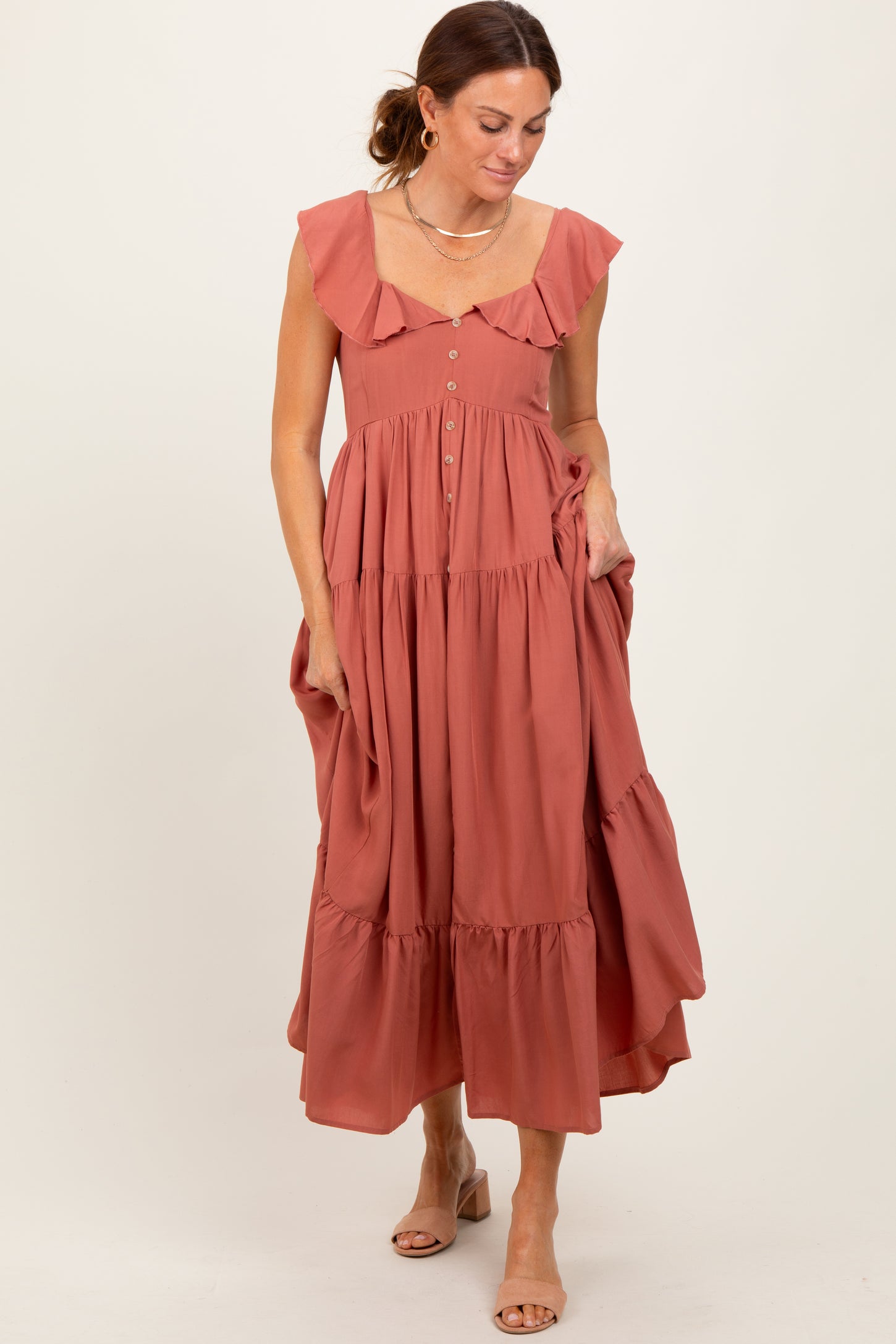 woman wearing a dusty rose ruffled midi dress with buttons and pockets, standing elegantly