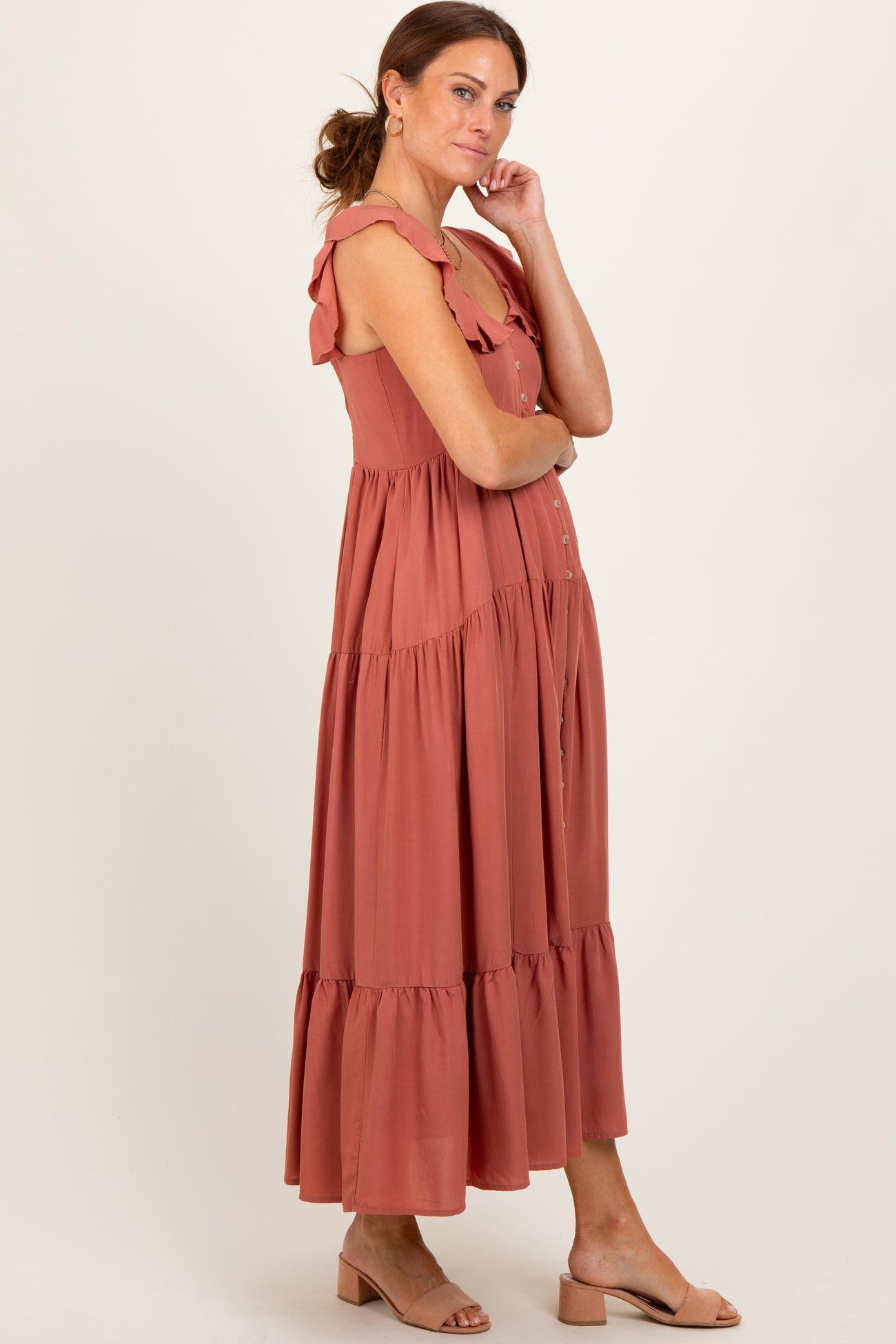 woman wearing a rust color maxi dress with ruffle straps and tiered hem, standing with hands on hips