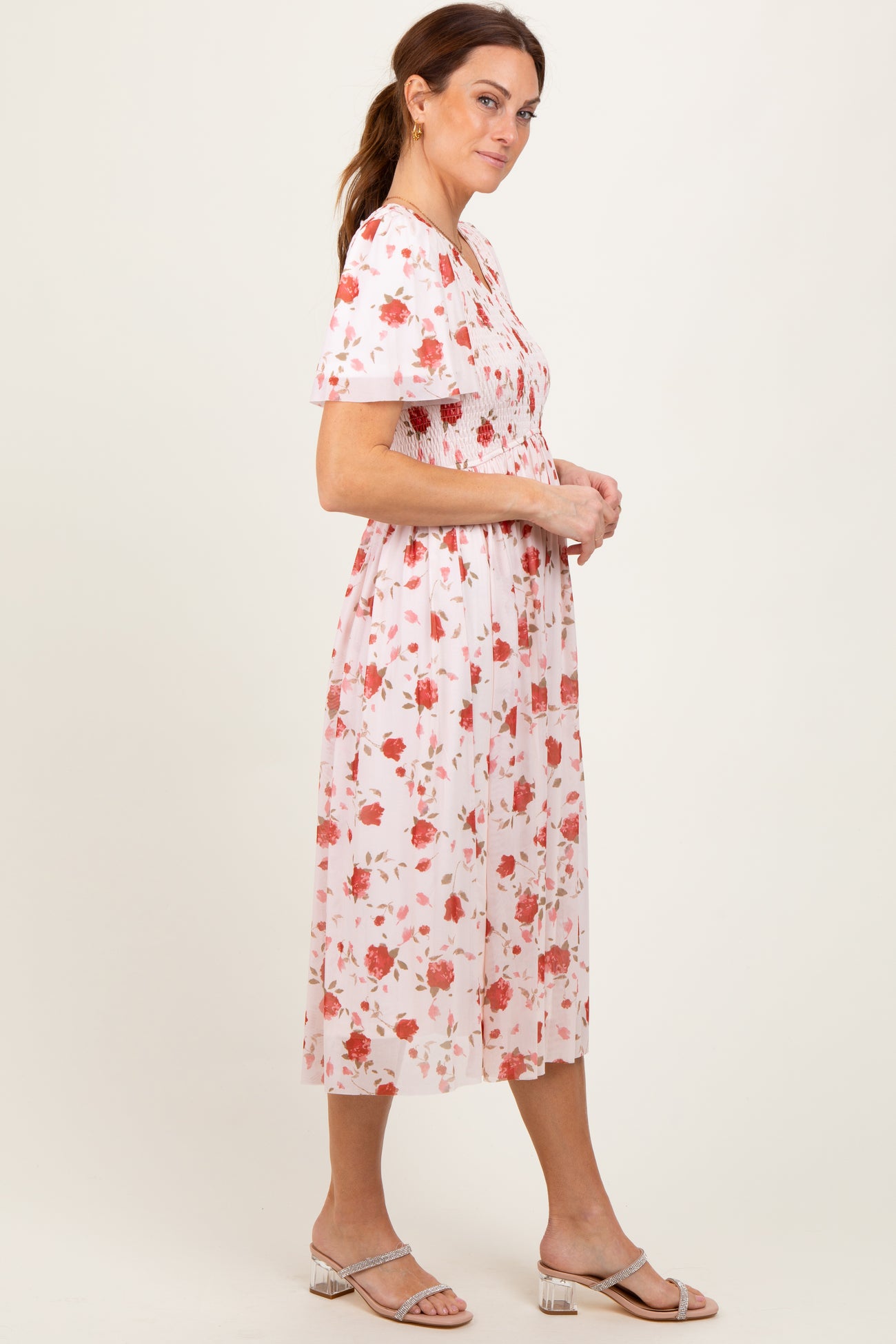 woman wearing a pink floral midi dress with short sleeves and a fitted bodice, standing sideways