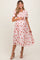 woman wearing a pink floral maternity dress with short sleeves and a smocked bodice, holding her baby bump
