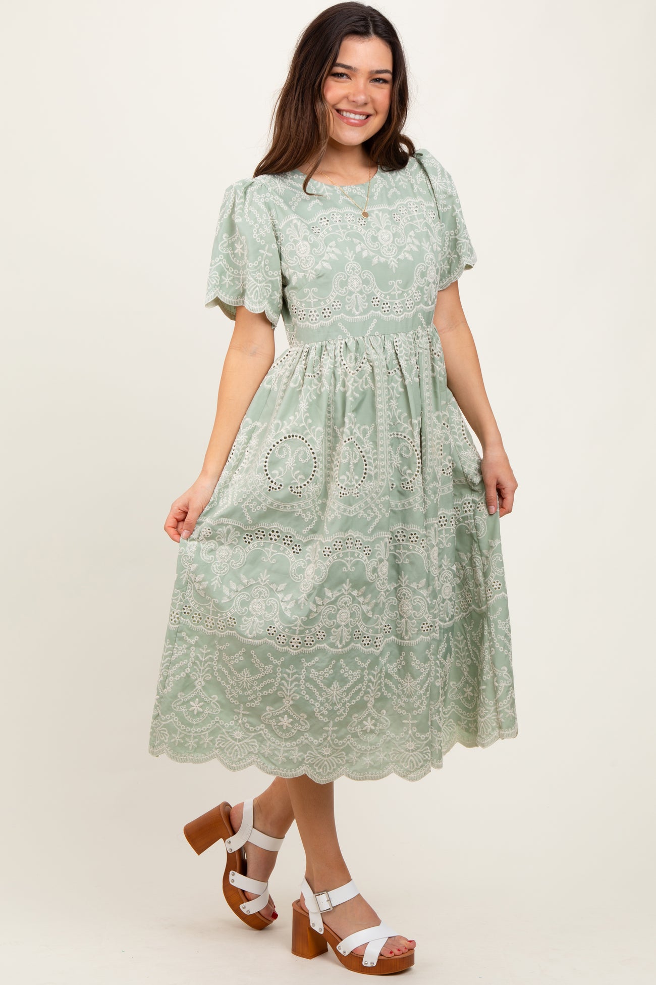 woman wearing a mint green embroidered midi dress with puff sleeves and a tiered skirt, paired with white platform sandals