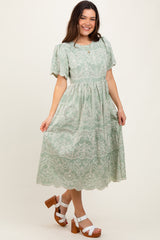 woman wearing a mint green embroidered midi dress with puff sleeves and a tiered skirt, paired with white platform sandals