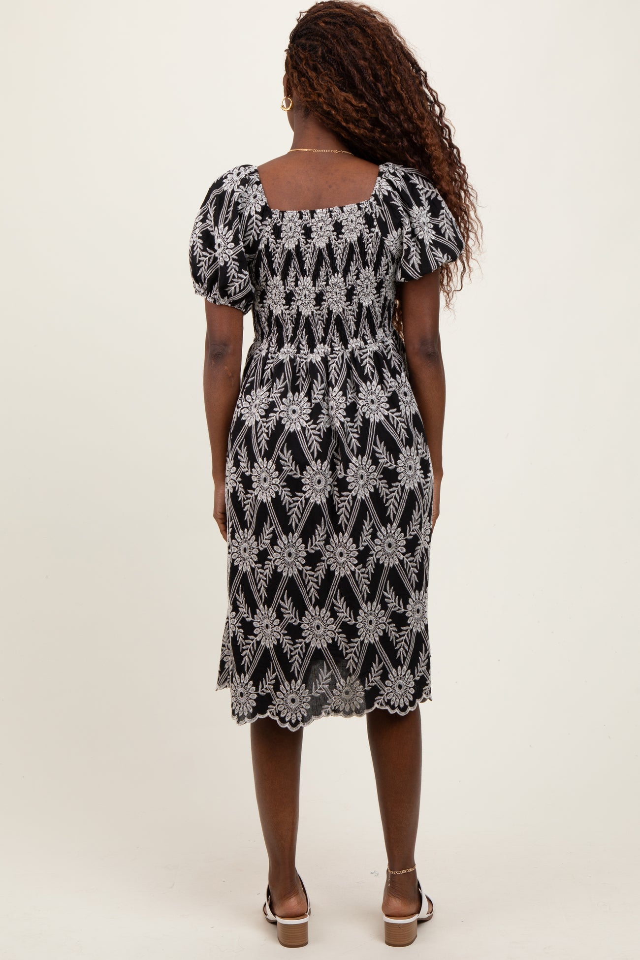 woman wearing a black floral embroidered midi dress with puff sleeves and a square back design