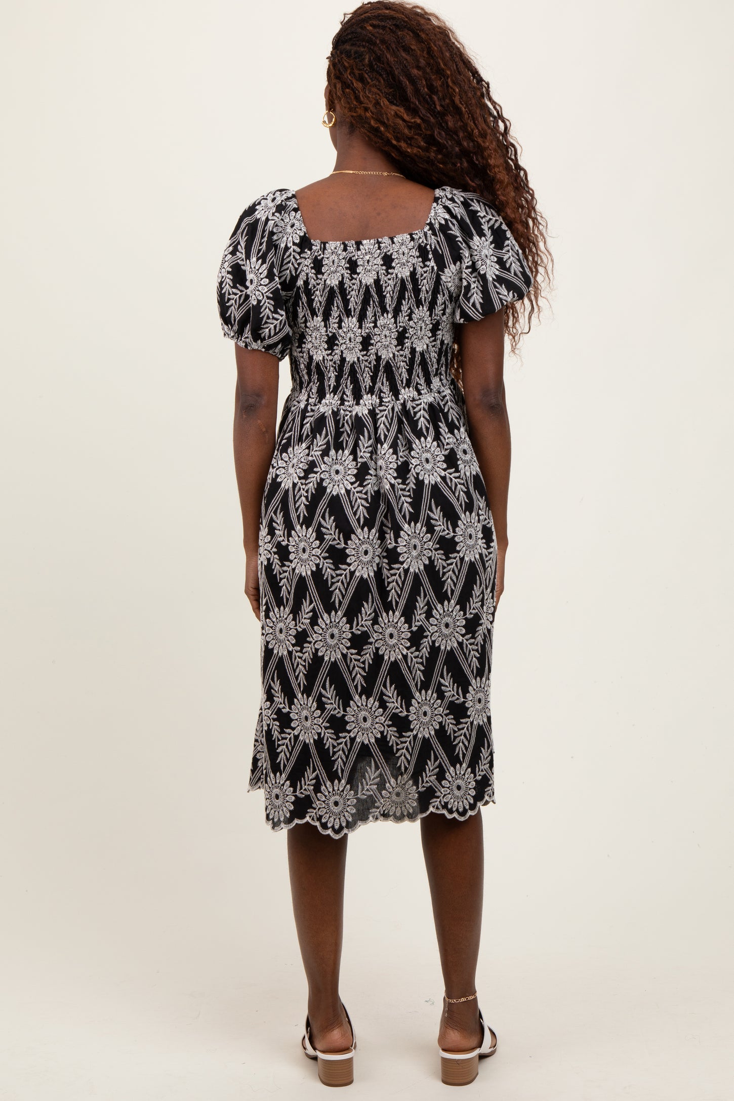woman wearing a black floral embroidered midi dress with puff sleeves and a square back design