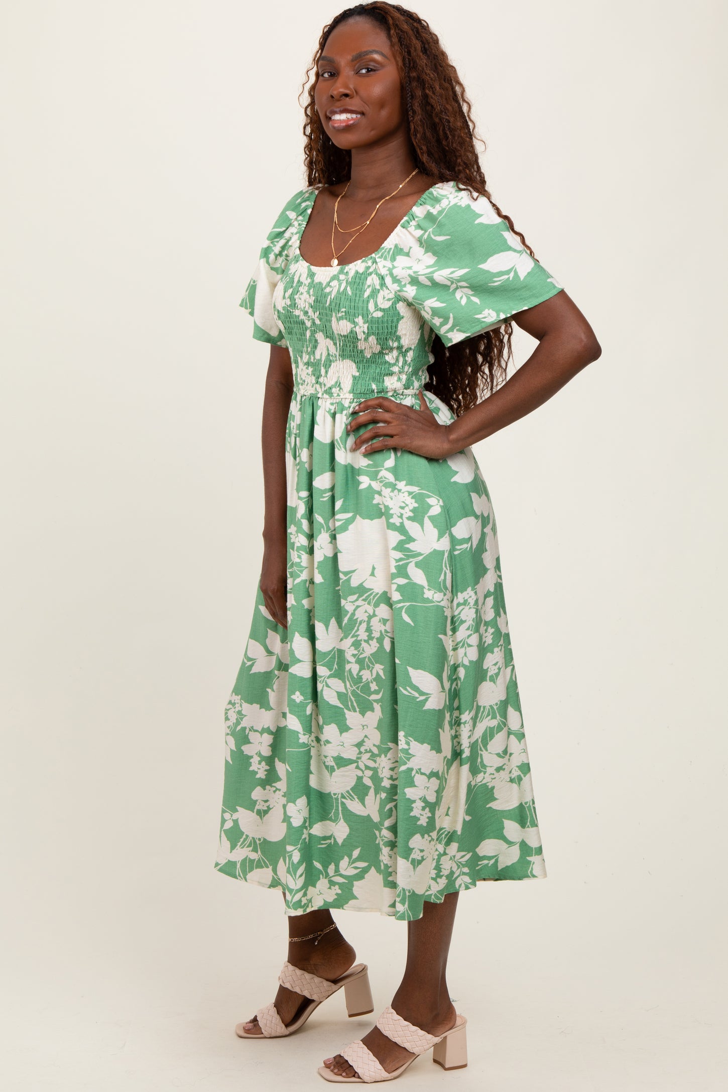 woman wearing a green floral midi dress with short puff sleeves and smocked bodice, standing with a smile
