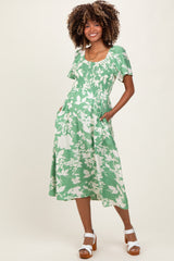 woman wearing a green floral maternity dress with short sleeves and pockets, showcasing her baby bump