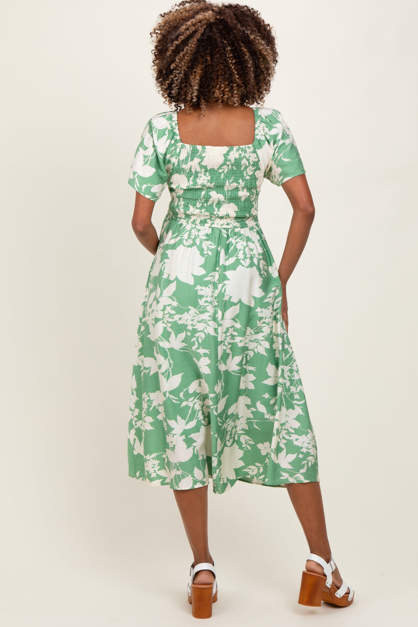 woman wearing a green floral maternity dress with short sleeves and a square back, showcasing a comfortable fit
