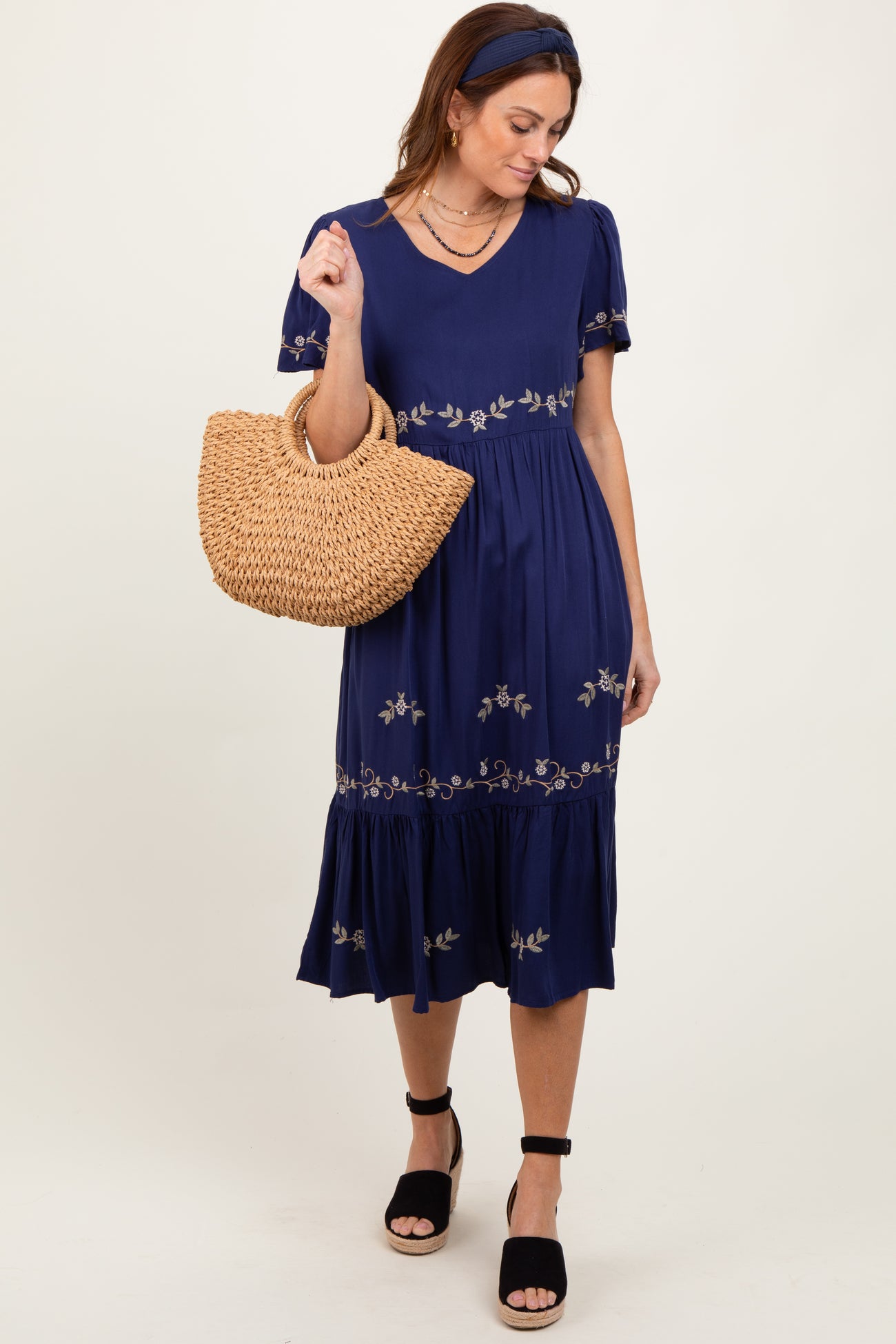 woman wearing a navy blue short sleeve dress with floral embroidery and holding a straw bag