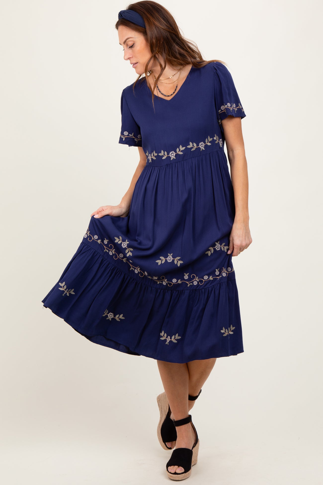 woman wearing a navy blue midi dress with floral embroidery and ruffled hem