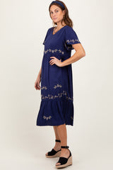 woman wearing a navy blue short sleeve dress with floral embroidery and a ruffled hem, standing in a relaxed pose