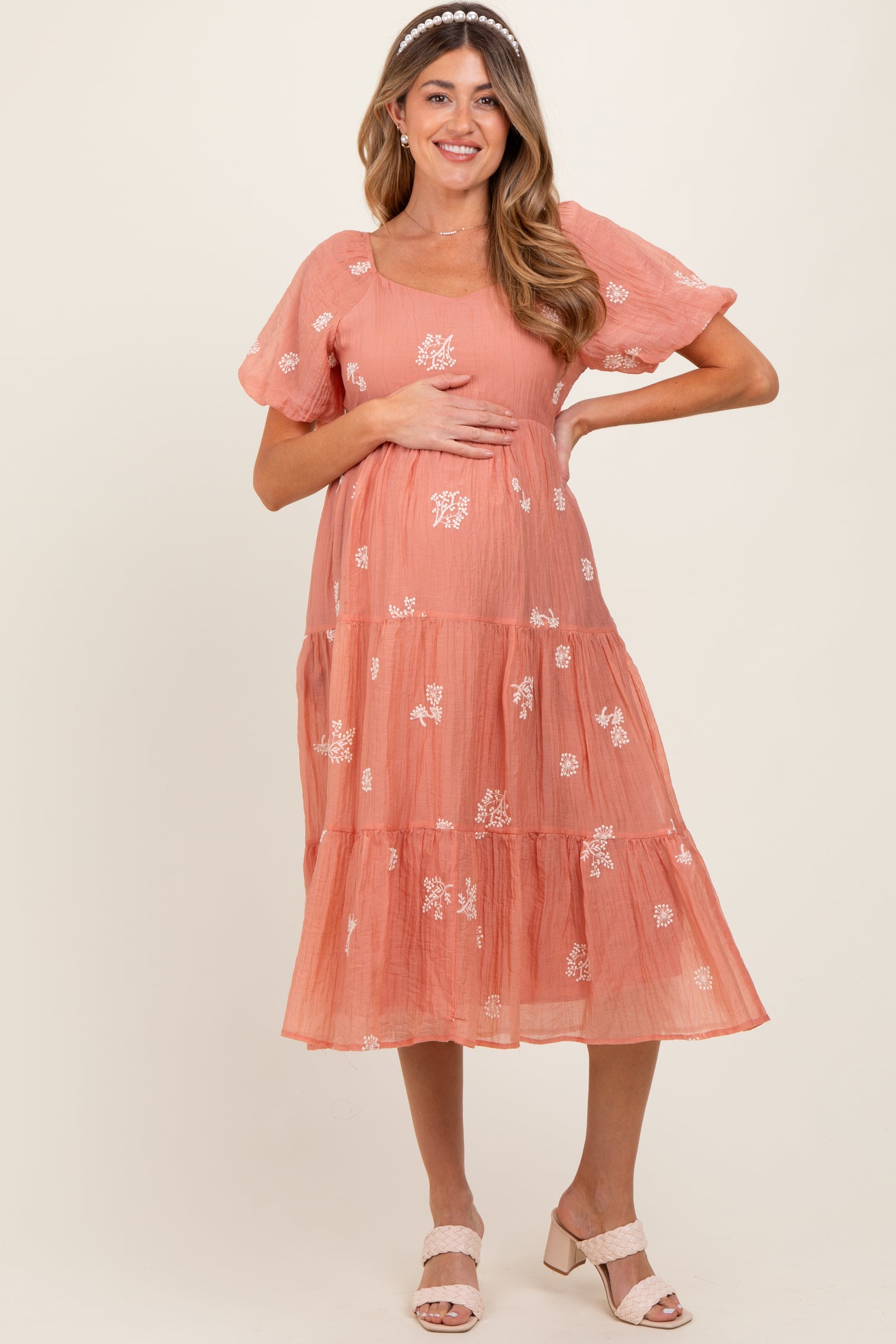woman wearing a peach tiered maternity dress with floral embroidery and holding her baby bump