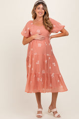 woman wearing a peach tiered maternity dress with floral embroidery and holding her baby bump