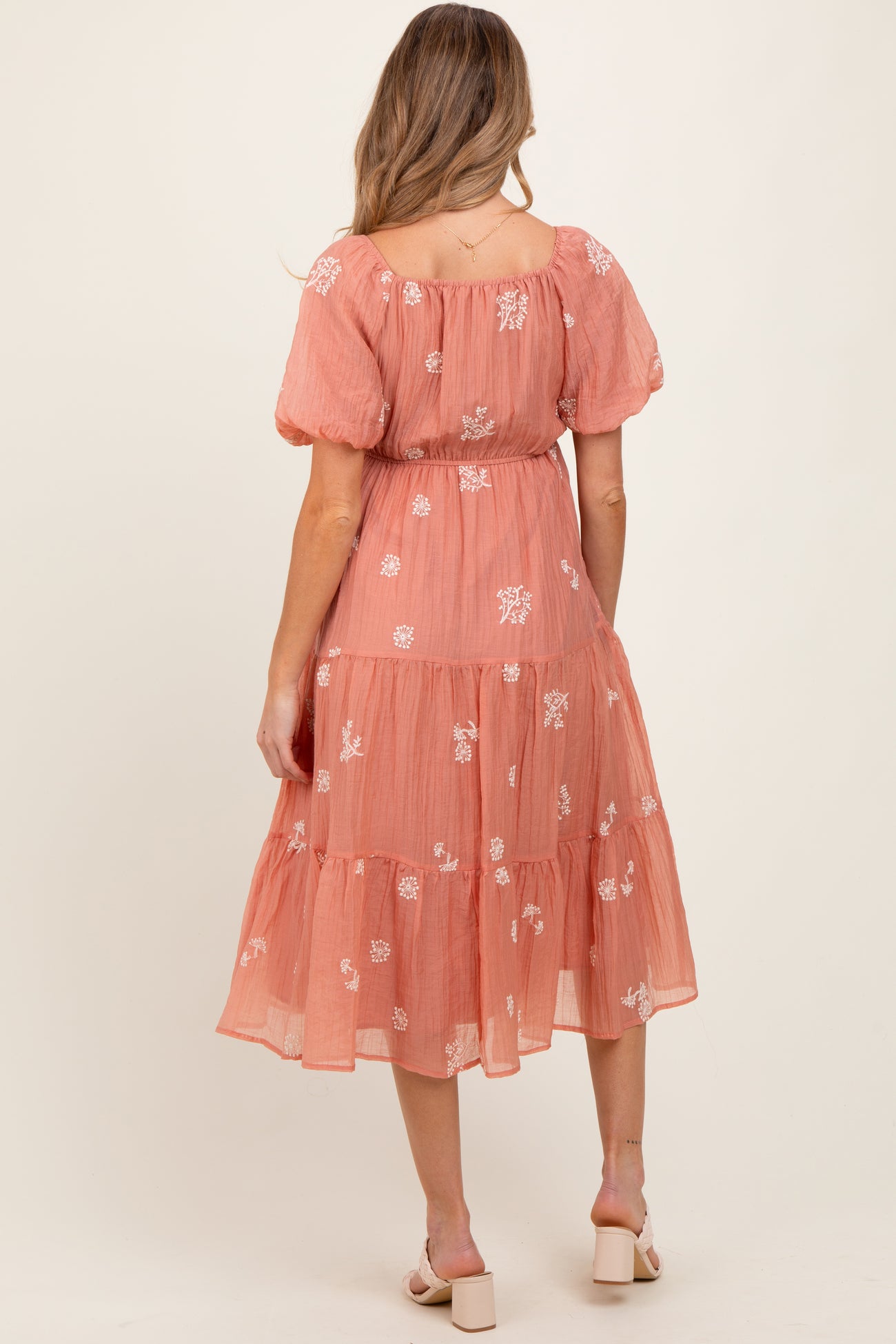 woman wearing a coral maternity dress with floral embroidery and tiered skirt, showing off her baby bump from the back