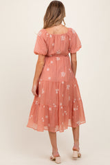 woman wearing a coral maternity dress with floral embroidery and tiered skirt, showing off her baby bump from the back