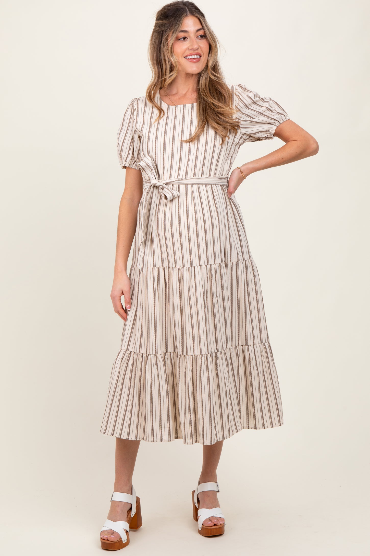 woman wearing a striped maternity dress with puff sleeves and a tie waist, showing her baby bump