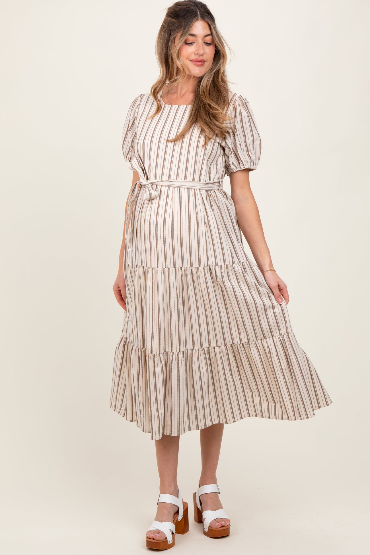 woman wearing a striped maternity dress with short puff sleeves and a tiered skirt, holding her baby bump