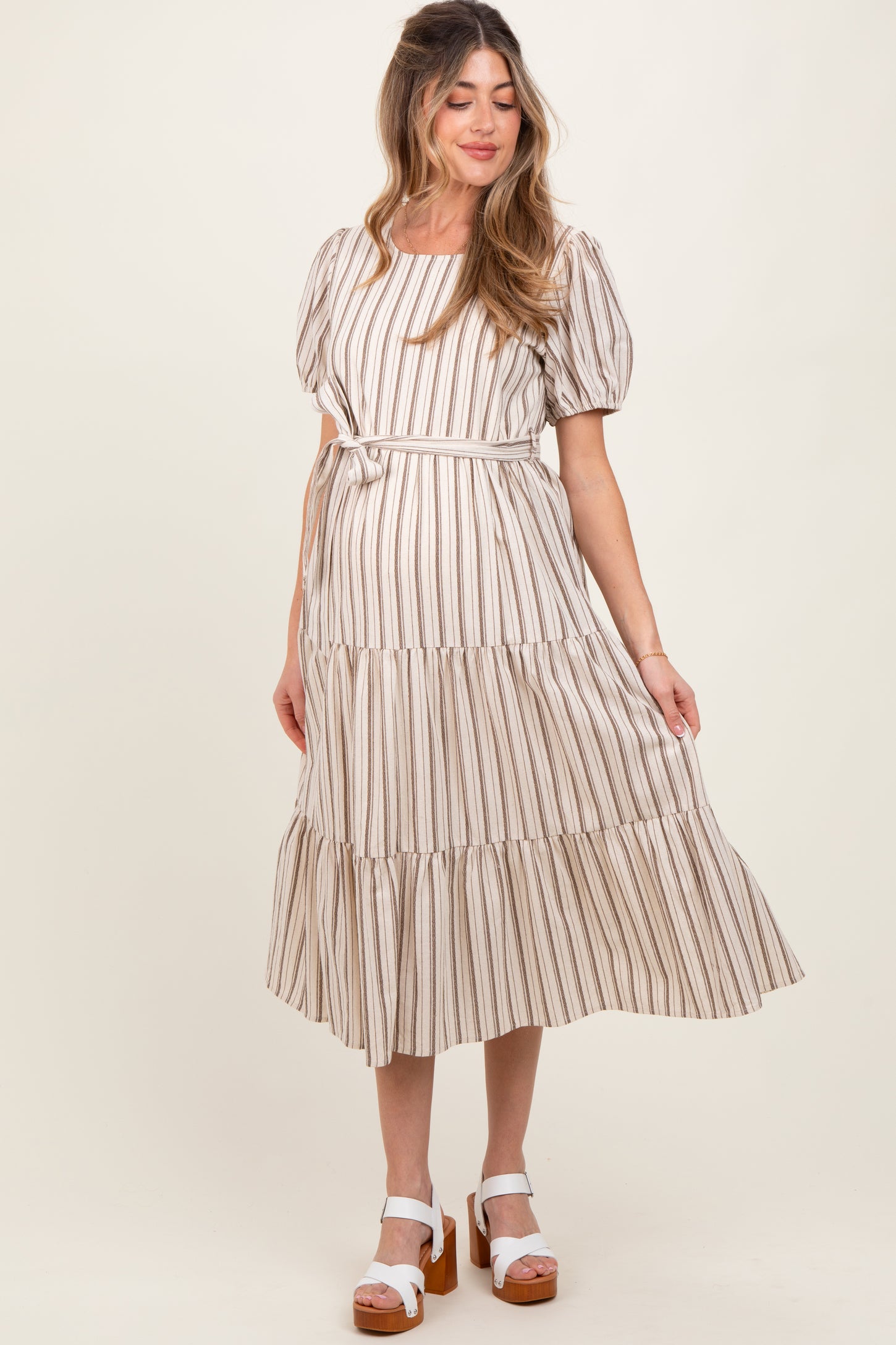 woman wearing a striped maternity dress with short puff sleeves and a tiered skirt, holding her baby bump