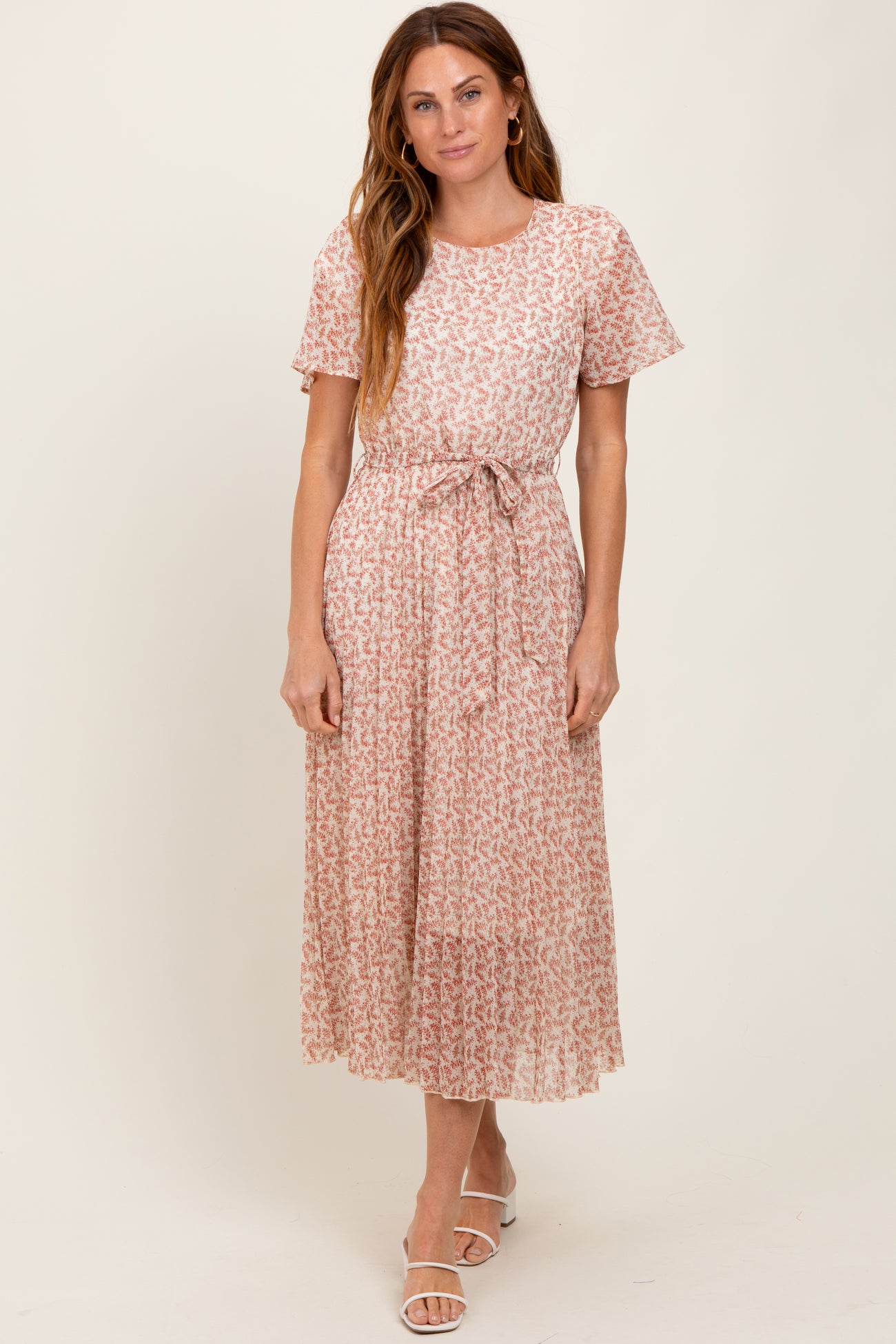 woman wearing a light pink floral midi dress with short sleeves and a tie belt at the waist