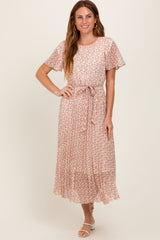 woman wearing a pink floral maxi dress with short sleeves and a tie belt, standing and smiling at the camera