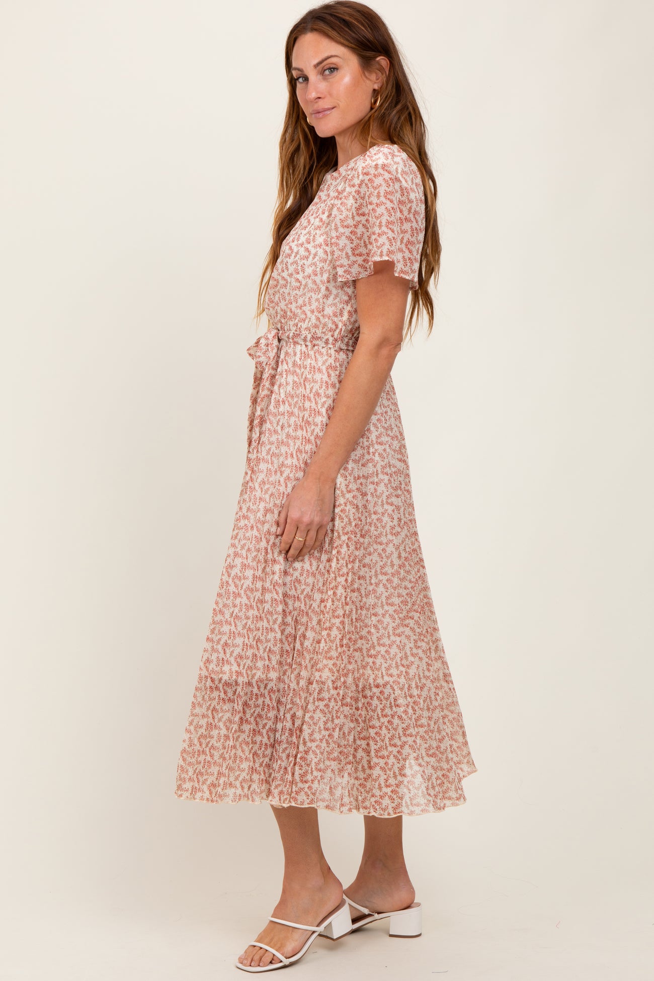 woman wearing a blush pink floral midi dress with short ruffled sleeves and a tie waist detail