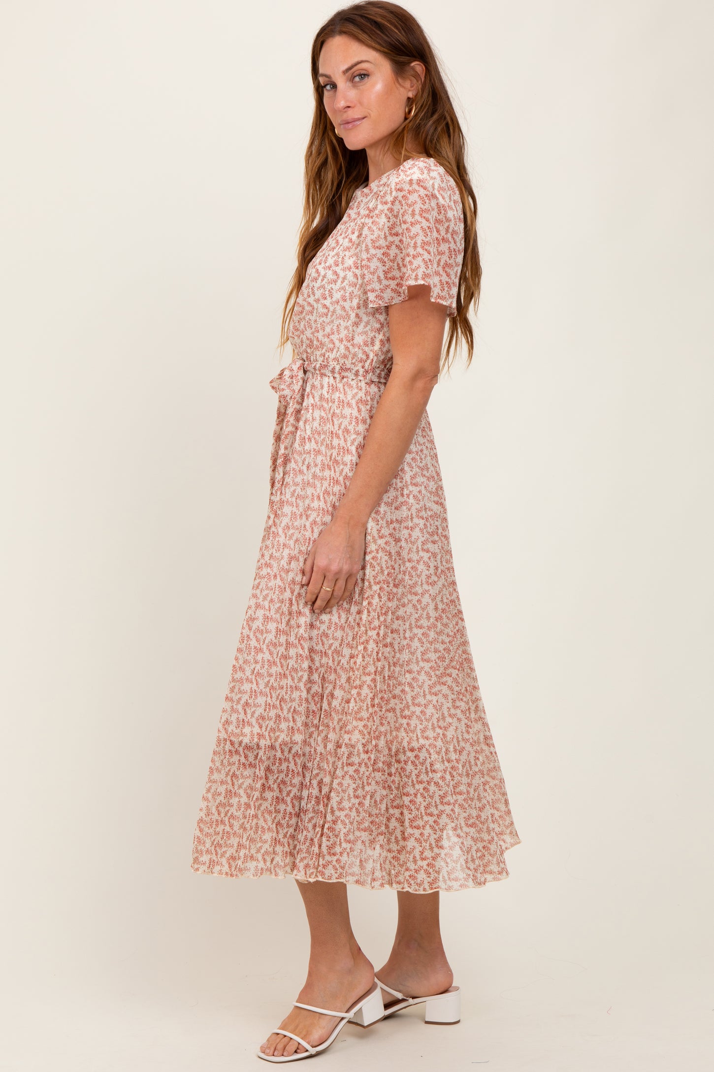 woman wearing a blush pink floral midi dress with short ruffled sleeves and a tie waist detail