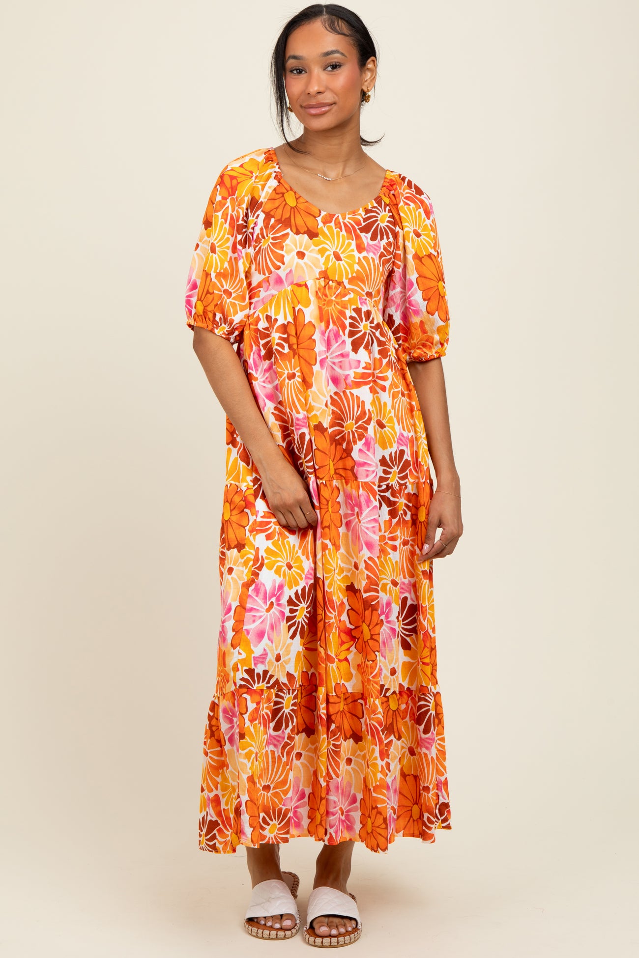 woman wearing a bright orange floral maxi dress with puff sleeves and tiered skirt, styled with white sandals