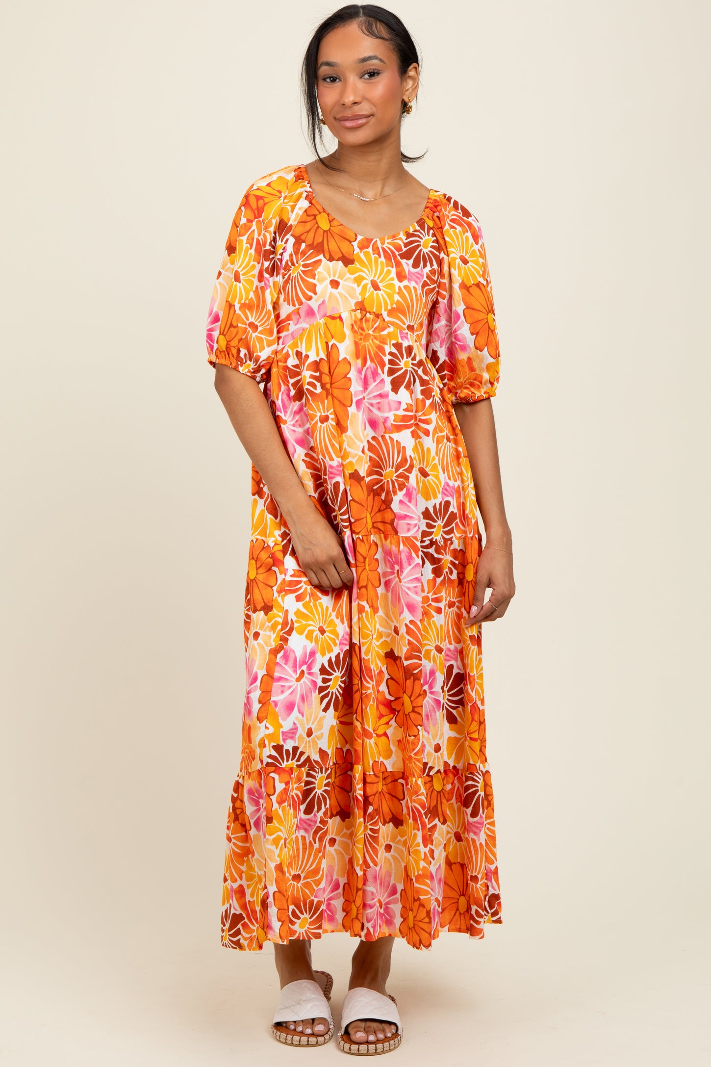 woman wearing a bright orange floral maxi dress with puff sleeves and tiered skirt, styled with white sandals