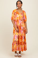 woman wearing a bright orange floral maxi dress with puff sleeves and tiered skirt, styled with white sandals