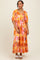 woman wearing a bright orange floral maxi dress with puff sleeves and tiered skirt, styled with white sandals