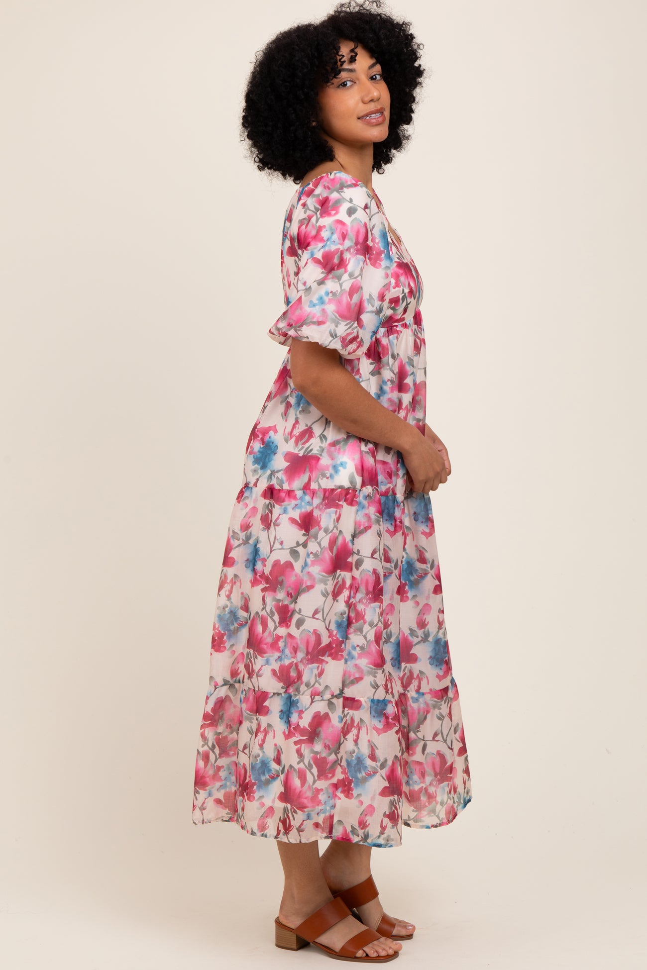 woman wearing a floral maxi dress with short puff sleeves in pink and blue tones, standing in profile