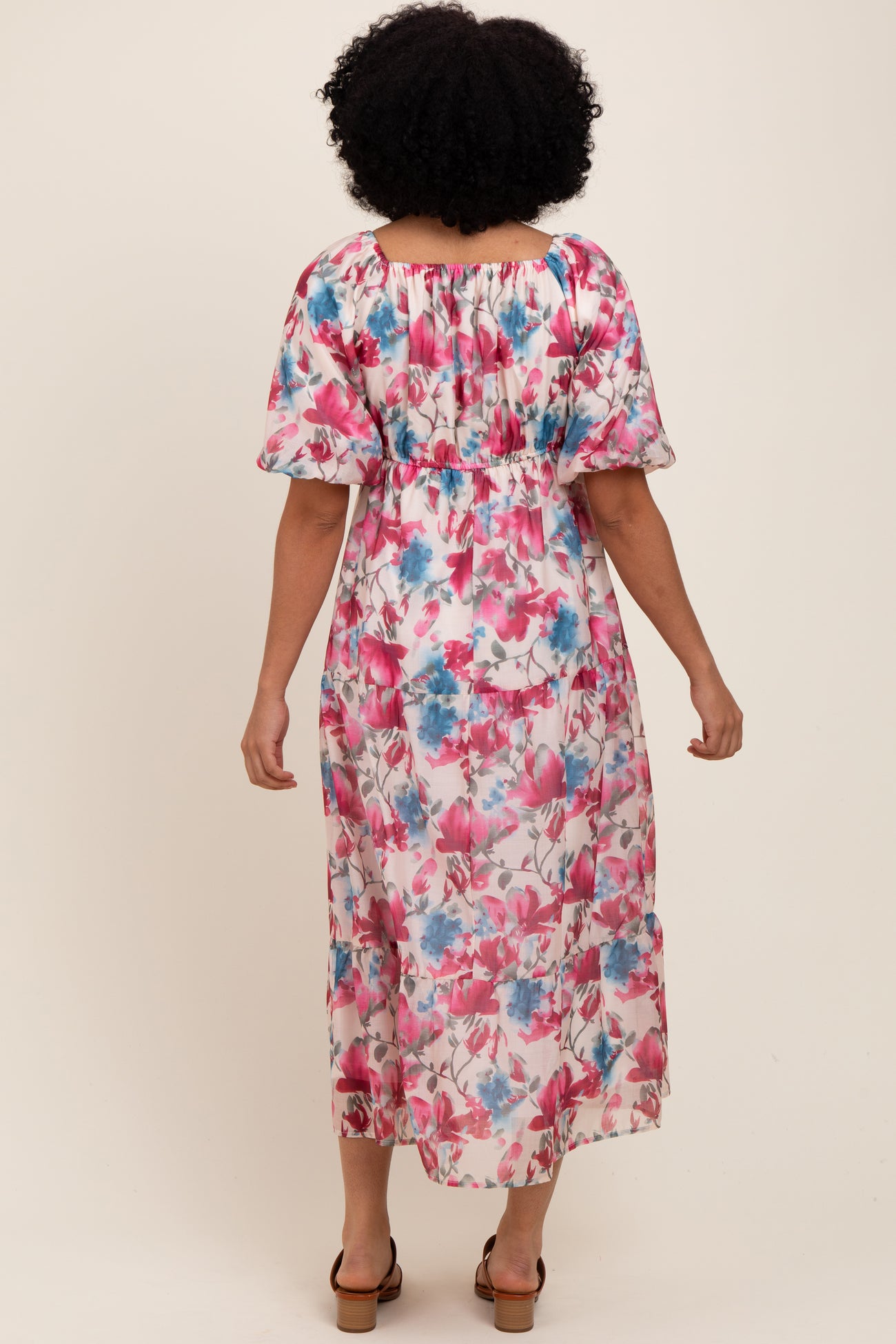 woman wearing a floral maxi dress with pink and blue flowers, featuring puff sleeves and a smocked waist, shown from the back