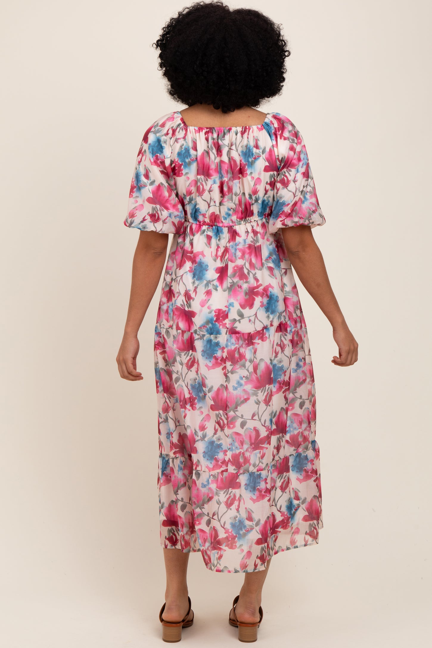 woman wearing a floral maxi dress with pink and blue flowers, featuring puff sleeves and a smocked waist, shown from the back