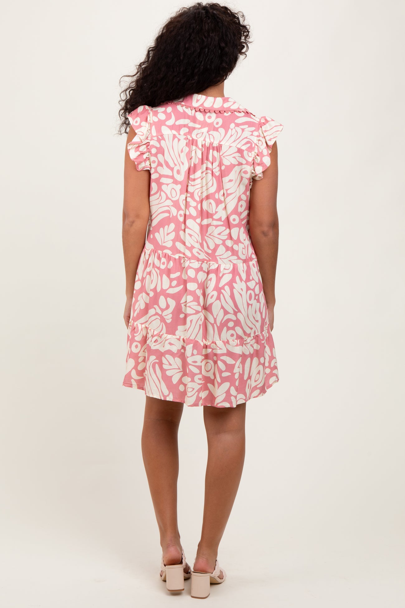 woman wearing a pink floral print short sleeve dress with ruffle details on the sleeves, seen from the back