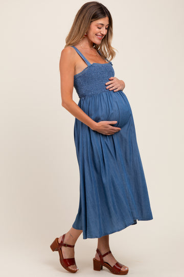 woman wearing a blue maternity maxi dress with a smocked bodice and holding her baby bump