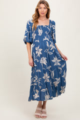 woman wearing a blue floral maternity maxi dress with puff sleeves and a tiered skirt, showcasing her baby bump