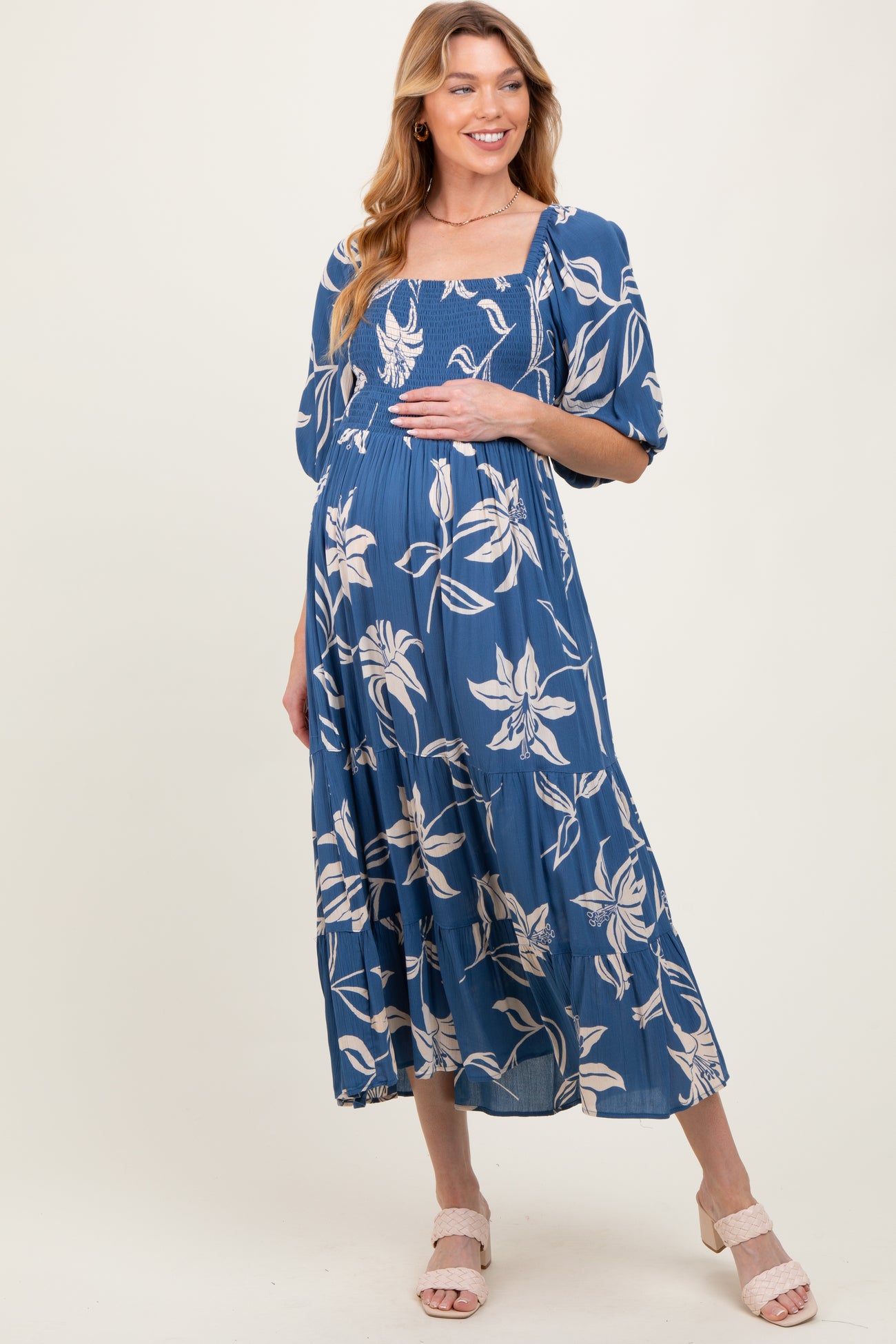 woman wearing a blue floral maternity dress with a smocked bodice and tiered skirt, holding her baby bump