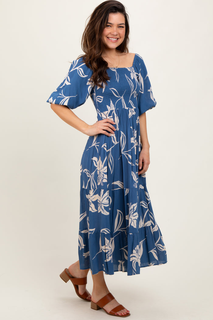 woman wearing a blue floral midi dress with puff sleeves and a smocked bodice, standing with a smile