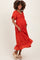 woman wearing an orange maternity dress with ruffle sleeves and hem, smiling and holding her baby bump
